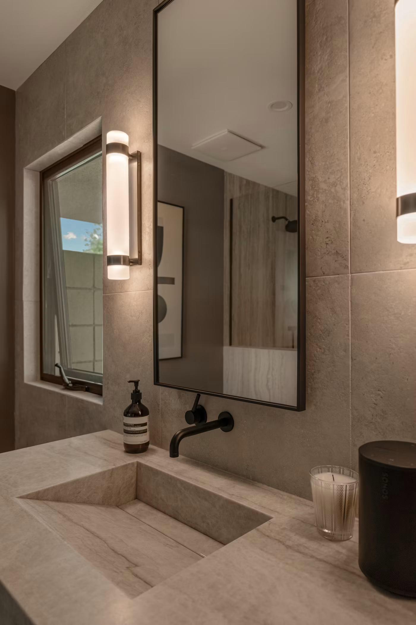 Stone vanity with wall-mounted faucet and backlit mirror