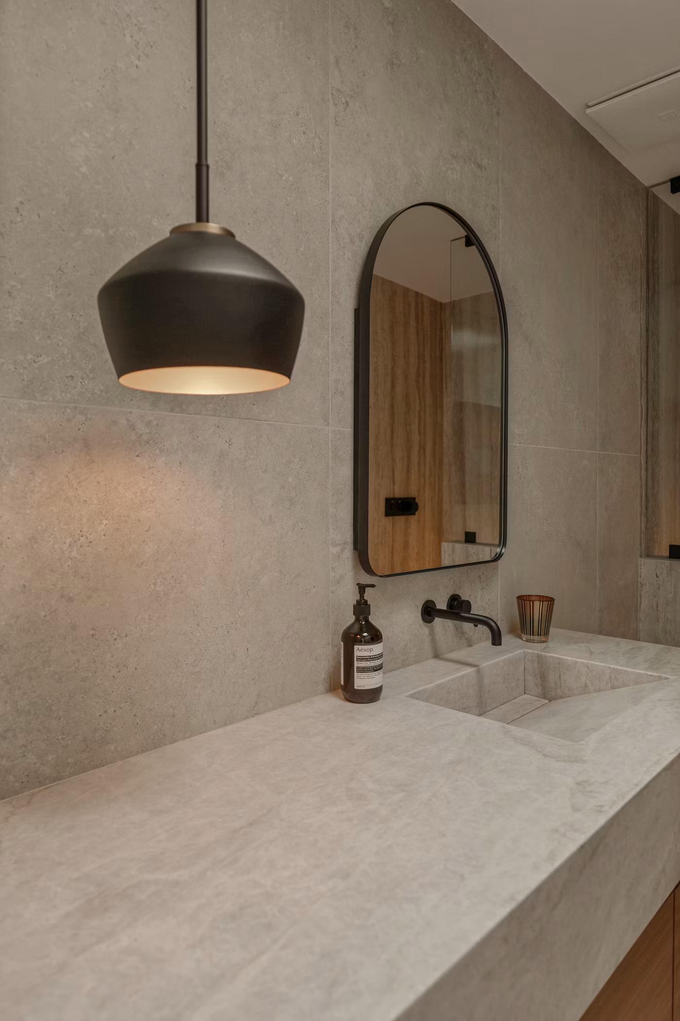 Arched mirror above stone vanity with pendant light