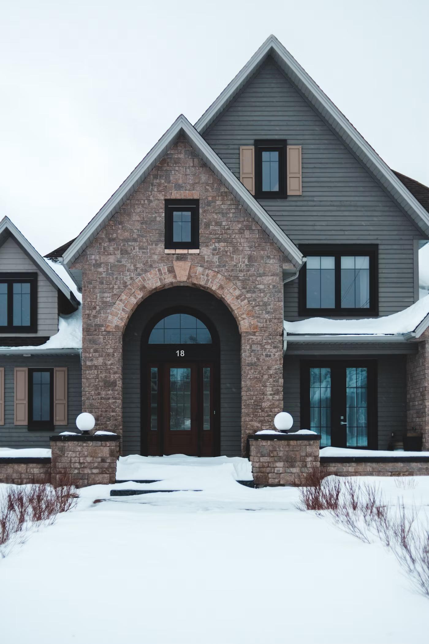 Two-story custom home exterior with stone entry arch in a winter landscape